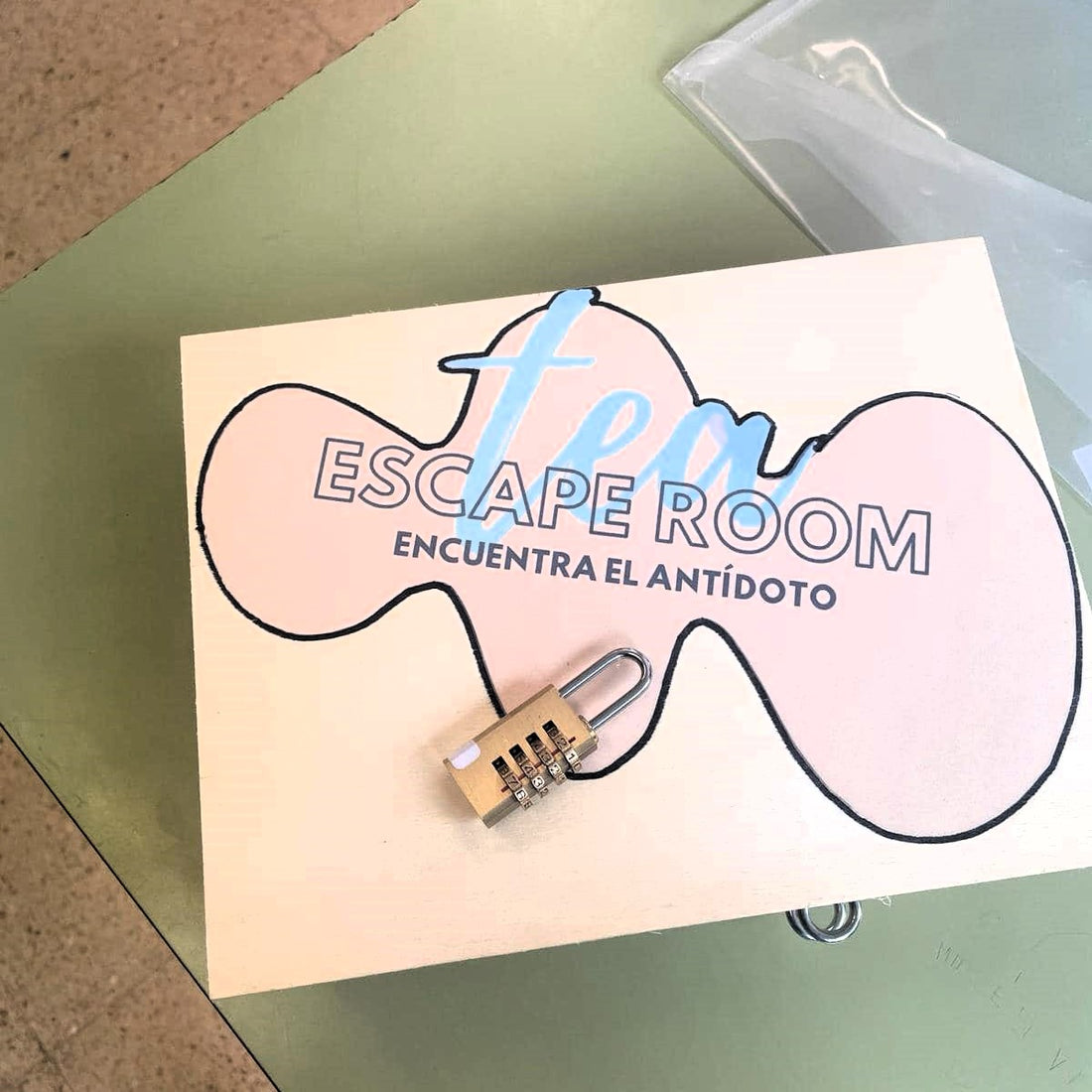 En primer plano, aparece una caja con el logo de la Escape Room y un candado sobre ella