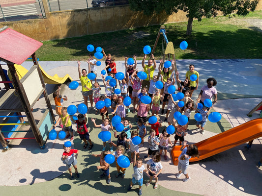 Un grupo de niños enfocados desde arriba tiran globos azules hacia arriba
