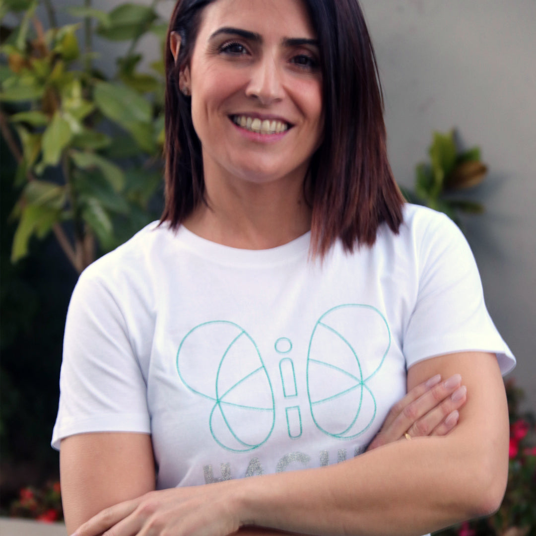 chica con camiseta blanca de manga corta con silueta grande de mariposa central en verde brillante y palabra HACHE en plateado debajo