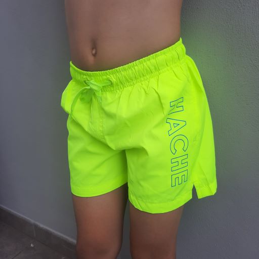 Primer plano de bañador infantil verde lima con la palabra HACHE escrita en color azul en sentido vertical en un lateral.