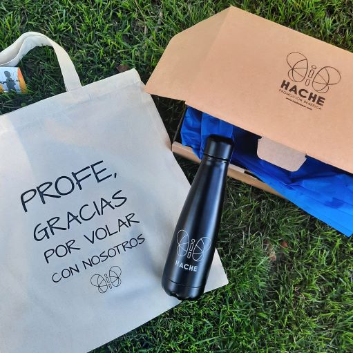 Botella negra con logo HACHE en silueta y tote bag con texto "profe, gracias por volar con nosotros"