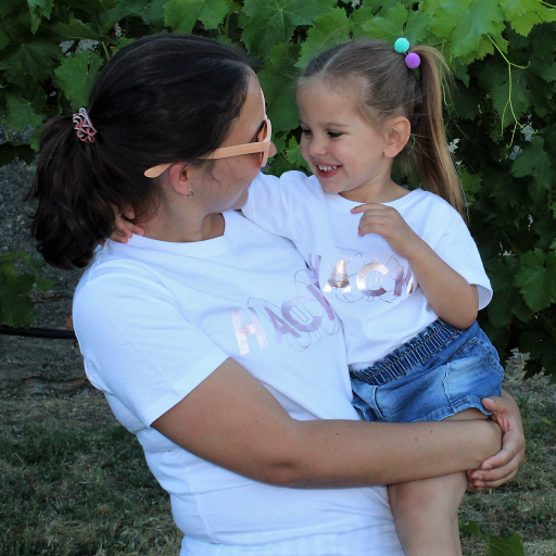 Foto de madre e hija con camiseta blanca con palabra HACHE escrita en rosa plateado y silueta de mariposa detrás.