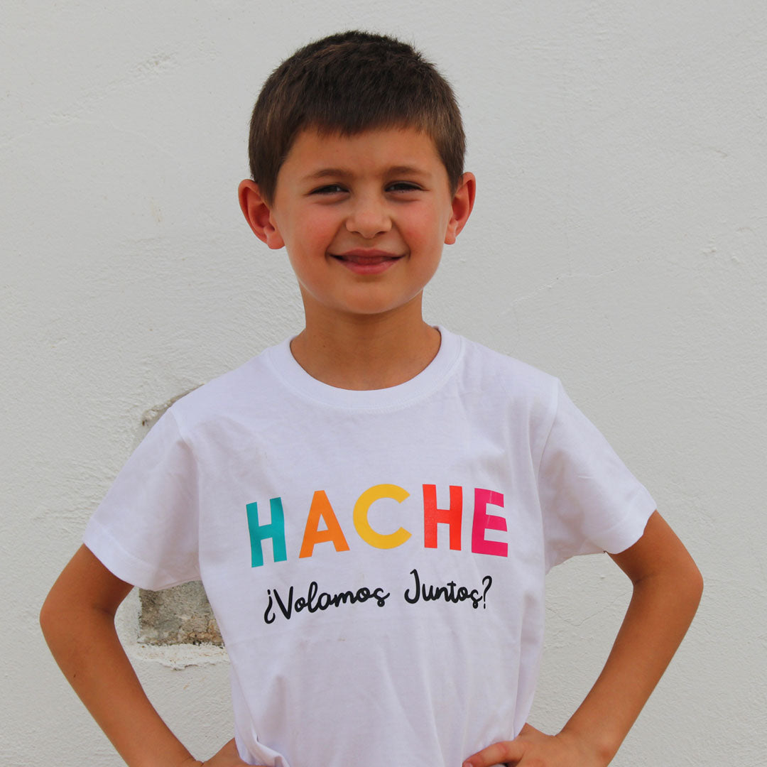 Niño con camiseta blanca. Palabra HACHE escrita en el pecho con un color de cada letra (azul, naranja, amarillo, rojo y rosa) y la pregunta ¿Volamos juntos? escrita en negro debajo
