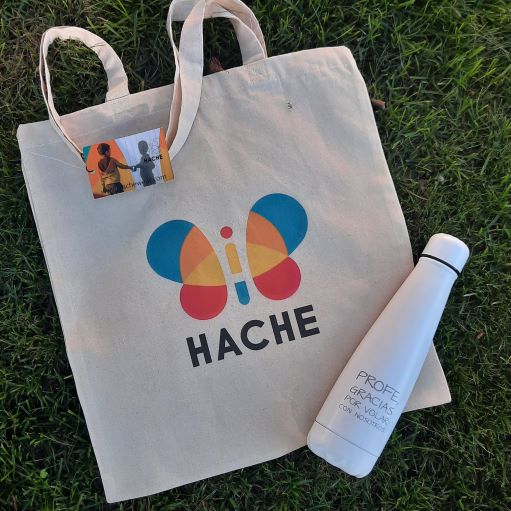 Tote bag con logo HACHE a color y botella blanca con texto "profe, gracias por volar con nosotros"
