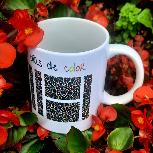 Taza blanca con figuras abstractas de colores que por su disposición espacial forman una Hache blanca en medio. Encima, la frase Gracias por llenar mis días de color.
