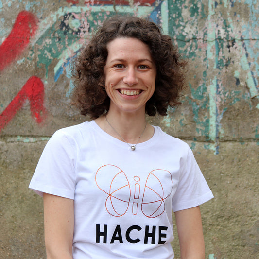 chica con camiseta blanca de manga corta con silueta grande de mariposa central en dorado y palabra HACHE en negro debajo