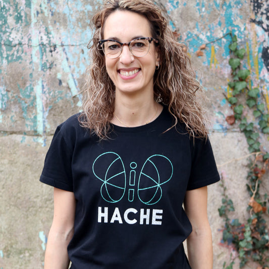 chica con camiseta negra de manga corta con silueta grande mariposa central en verde brillante y palabra HACHE en plateado debajo
