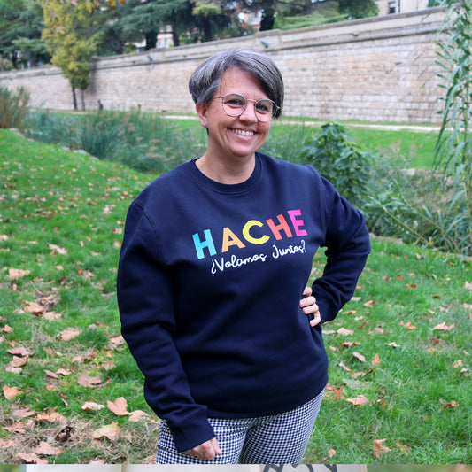 Mujer viste una sudadera azul marino con letras HACHE en multicolor y la frase ¿volamos juntos? en blanco debajo de la palabra
