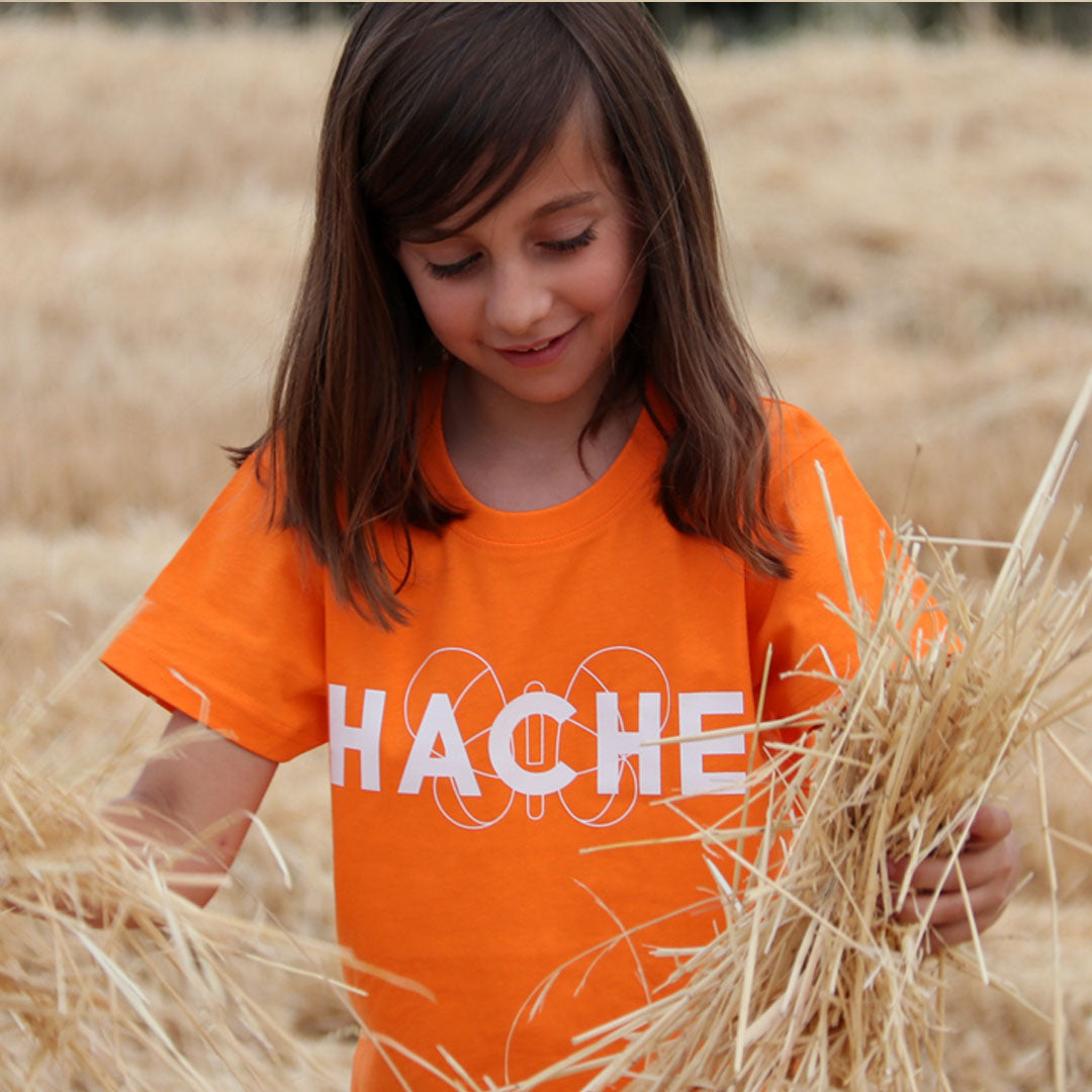 Niña con camiseta naranja y palabra HACHE escrita en blanco en el pecho con silueta de mariposa detrás