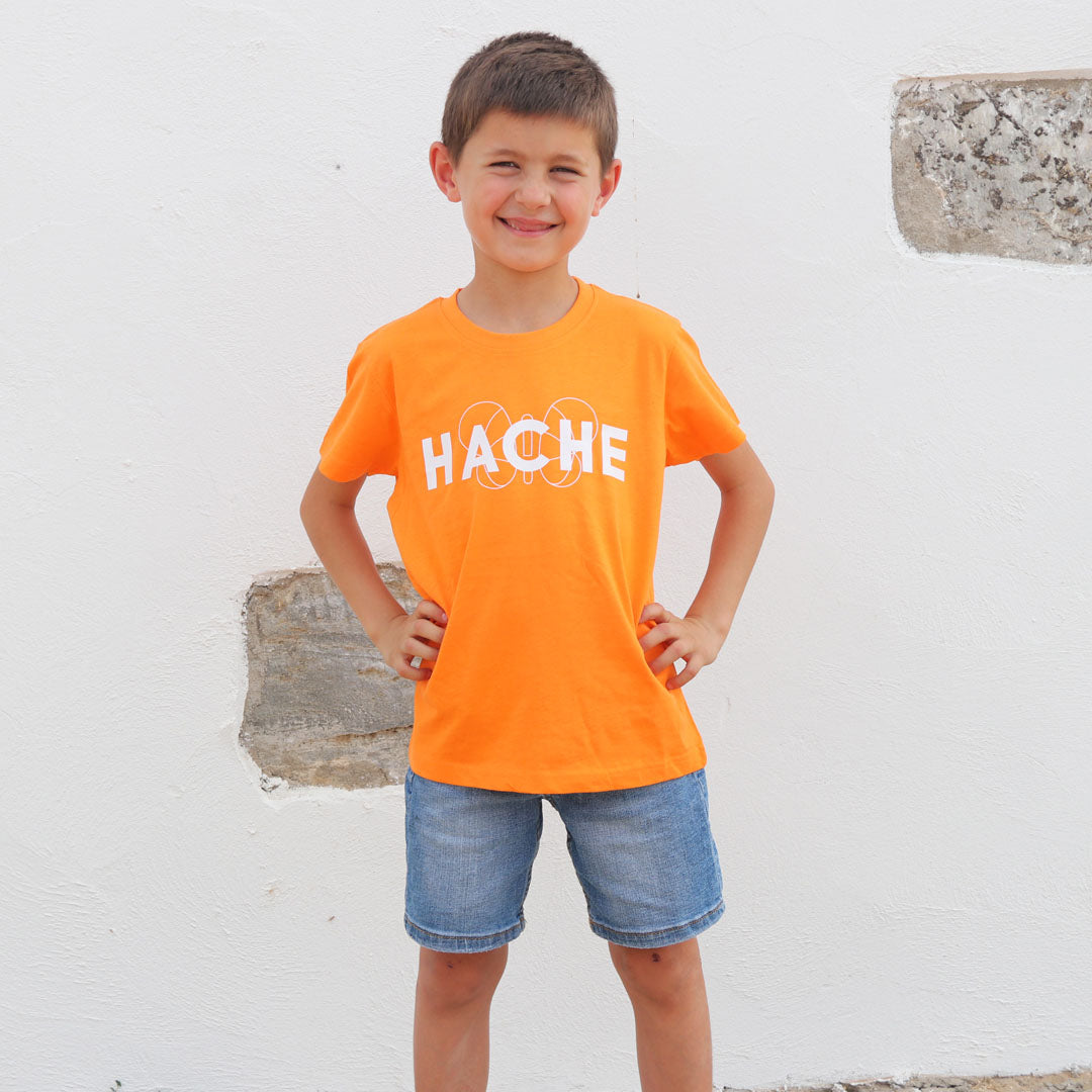 Niño con camiseta naranja y palabra HACHE escrita en blanco en el pecho con silueta de mariposa detrás
