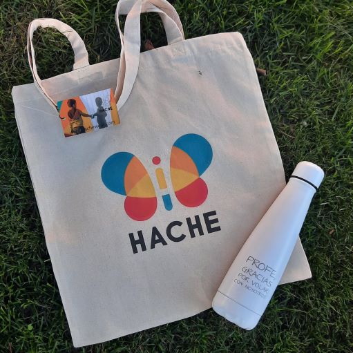 Tote bag con logo HACHE a color y botella blanca con texto  "profe, gracias por volar con nosotros"