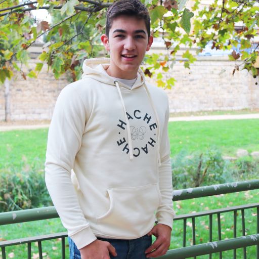 Chico joven con sudadera crema y círculo hecho con las letras de la palabra Hache y una mariposa en silueta en el centro.