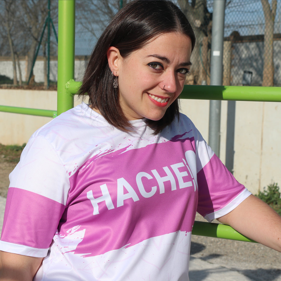 camiseta deportiva unisex blanca con franja central horizontal rosa y palabra HACHE en blanco sobre la franja
